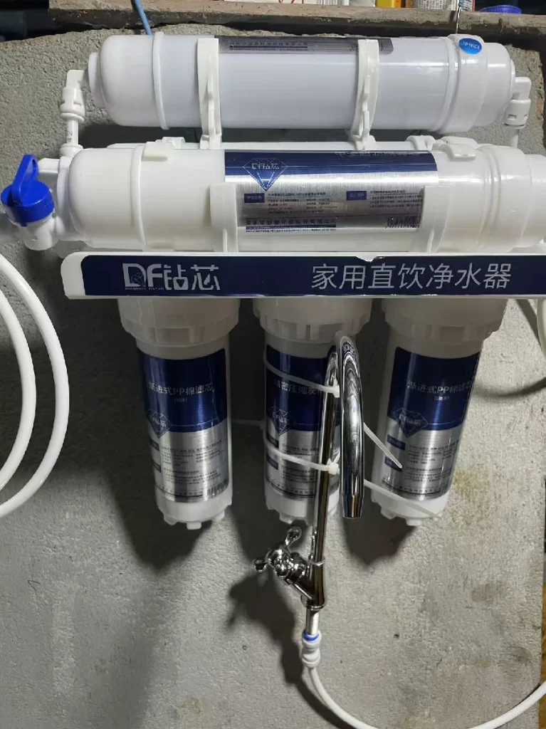 A three-stage ultrafiltration water purifier installed on a concrete wall.
